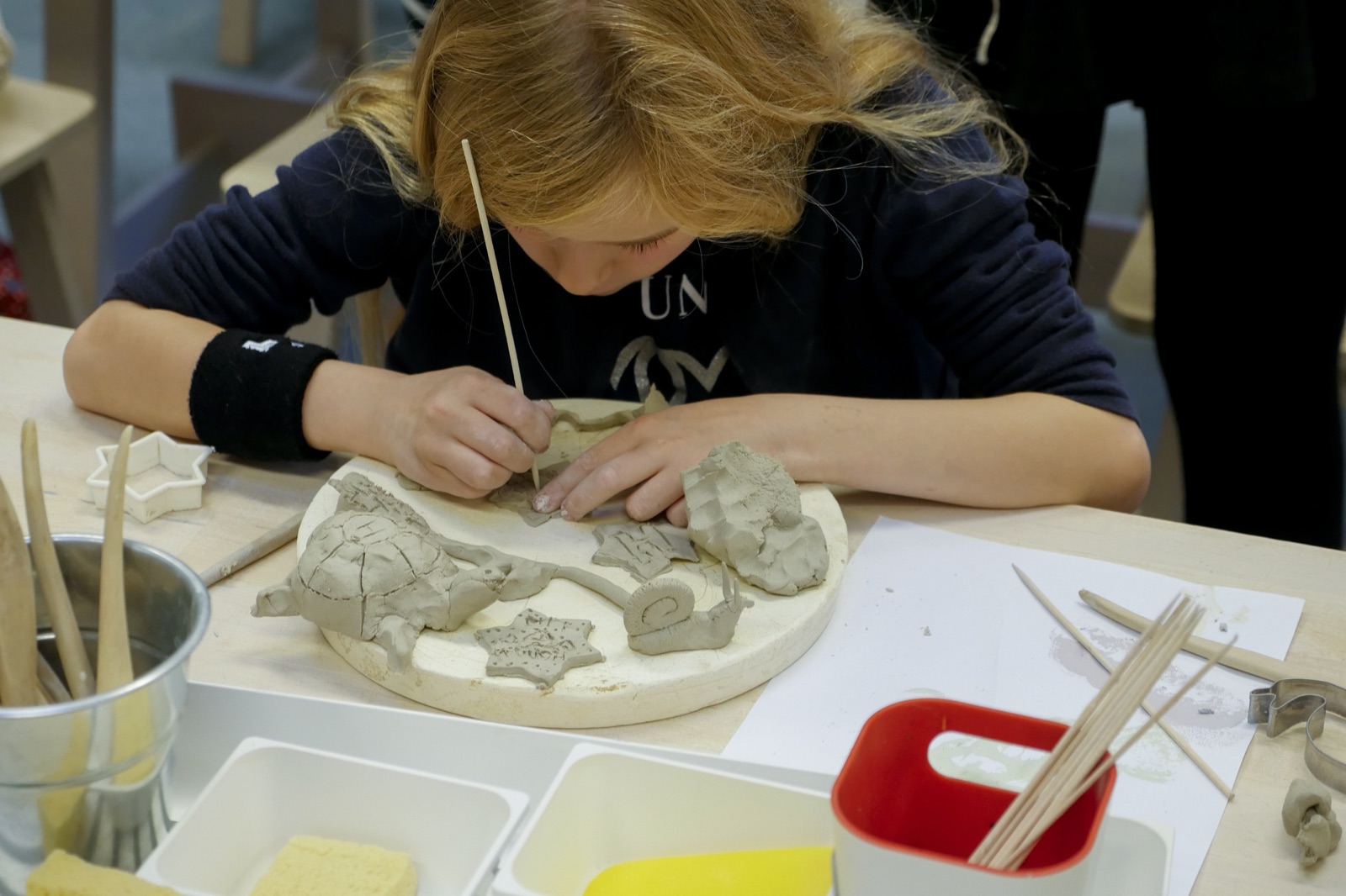 A child intently shapes clay figures with a modelling tool