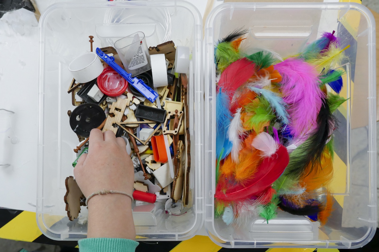 A hand chooses between building parts and colourful feathers for a project