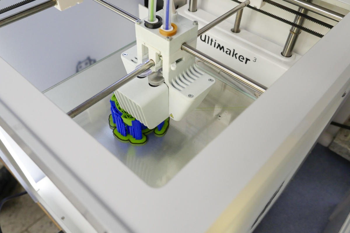 Ein 3D-Drucker fertigt ein kleines Modell in Blau und Grün